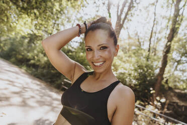 Woman with hand in hair smiling while standing at park - MFF07125