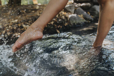 Mature woman splashing water with barefoot at park - MFF07129