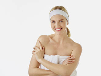 Smiling woman wearing headband and towel standing with arms crossed against white background - RORF02588