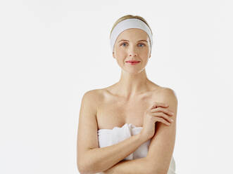 Young woman with headband wrapped in towel staring while standing against white background - RORF02589