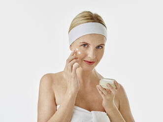 Woman applying face cream while standing against white  background - RORF02592