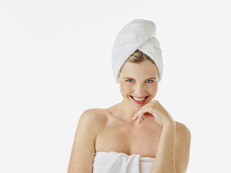 Smiling woman wrapped in towel staring while standing against white background - RORF02593