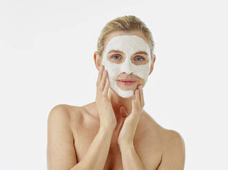 Frau, die eine Gesichtsmaske aufträgt, während sie vor einem weißen Hintergrund steht - RORF02602