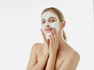Junge Frau starrt beim Anlegen einer Gesichtsmaske auf weißem Hintergrund - RORF02603