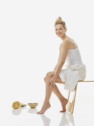 Lächelnde Frau sitzt auf einem Stuhl vor weißem Hintergrund - RORF02604
