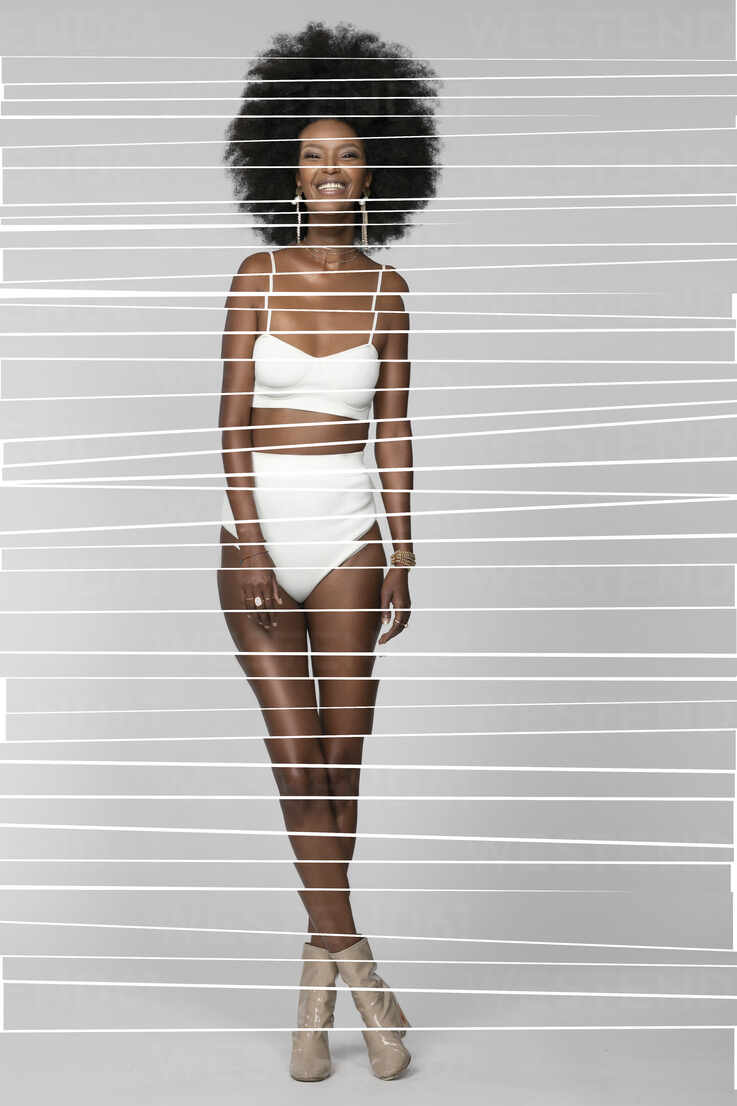 Smiling Afro woman with legs crossed standing against white