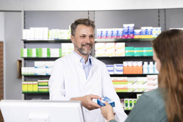 Lächelnder Mann, der einer Kundin an der Apothekenkasse ein medizinisches Rezept ausstellt - FKF03960