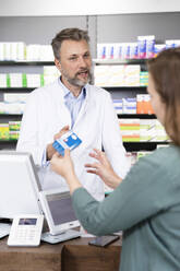 Mature pharmacist advising customer about medicine at checkout in store - FKF03961