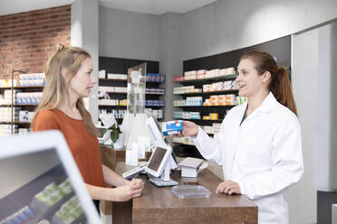 Female pharmacist advising medicine prescription to woman at checkout in store - FKF03973
