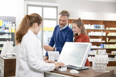 Female pharmacist billing while customers standing at pharmacy checkout - FKF03987