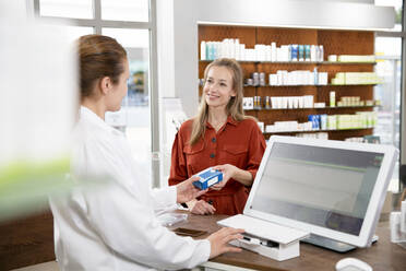 Eine Apothekerin gibt einer Frau an der Kasse im Laden ein Medikament - FKF03990