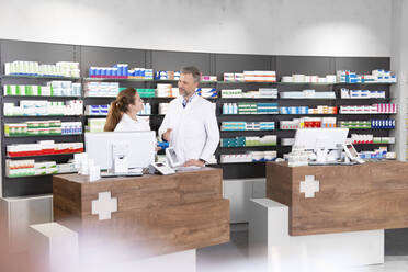 Apothekerin mit männlichem Kollegen im Gespräch am Apothekentresen - FKF03994