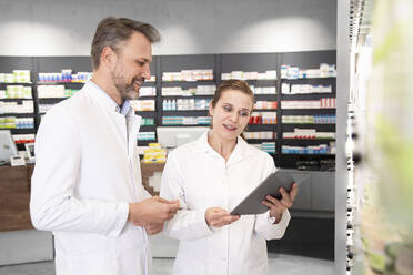 Female pharmacist with digital tablet discussing with male colleague - FKF04004