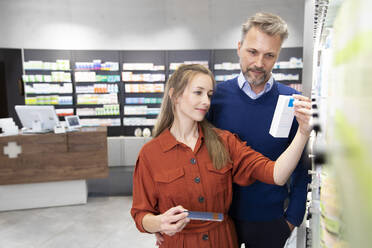 Frau hält verschreibungspflichtige Medikamente in der Hand, während sie mit einem Mann in einer Apotheke steht - FKF04008
