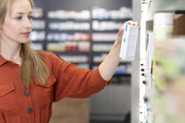 Female customer reading instructions on medicine box at pharmacy - FKF04011