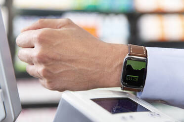 Männlicher Kunde beim kontaktlosen Bezahlen mit einer Smartwatch in einer Apotheke - FKF04012