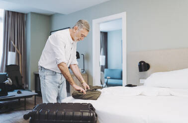 Man unpacking suitcase while standing in bedroom at hotel - DGOF01911