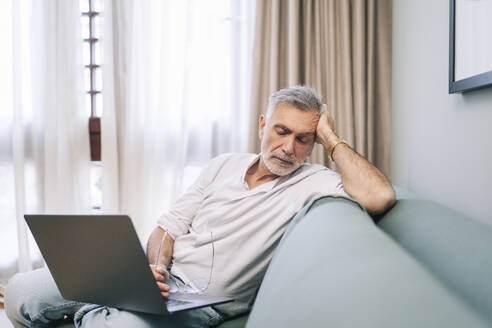 Erschöpfter Mann mit Laptop auf dem Sofa im Hotelzimmer - DGOF01920