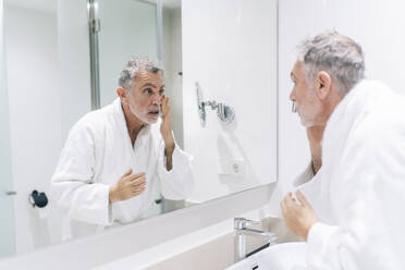 Surprised man wearing bathrobe looking at mirror in hotel bathroom - DGOF01935
