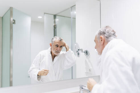 Handsome man looking at reflection in mirror of hotel bathroom - DGOF01936