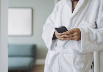 Mann im Bademantel benutzt Smartphone im Hotelzimmer - DGOF01938