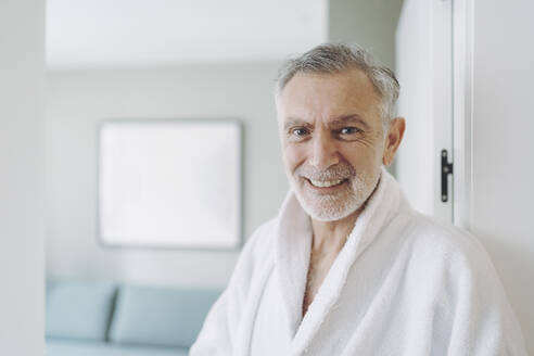 Happy man in bathrobe at hotel room - DGOF01940