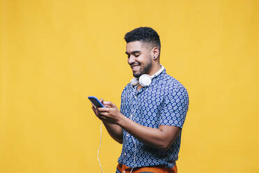Lächelnder Mann mit Mobiltelefon vor gelbem Hintergrund - DGOF01947