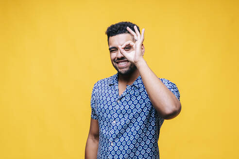 Happy man showing OK gesture while standing against yellow background - DGOF01953