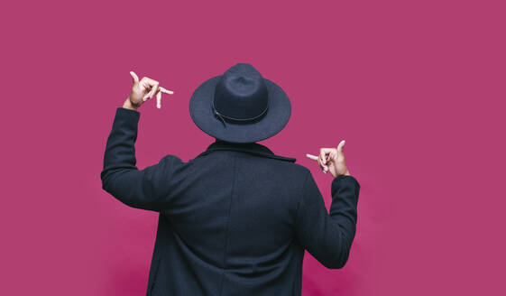 Man in blazer jacket gesturing in front of pink background - DGOF01961