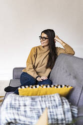 Young woman looking away while sitting on sofa at home - GIOF11178