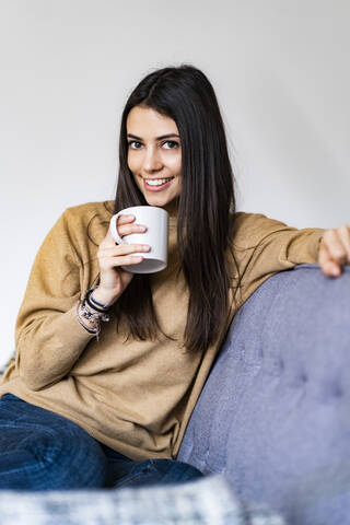 Frau trinkt Kaffee, während sie zu Hause auf dem Sofa sitzt, lizenzfreies Stockfoto