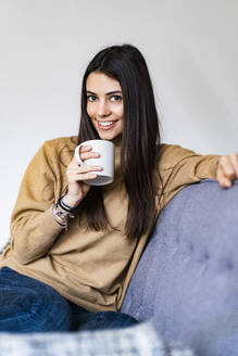 Frau trinkt Kaffee, während sie zu Hause auf dem Sofa sitzt - GIOF11189