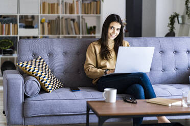 Smiling woman using laptop while sitting at home - GIOF11190