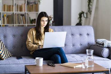 Junge Frau, die zu Hause sitzend am Laptop arbeitet - GIOF11193