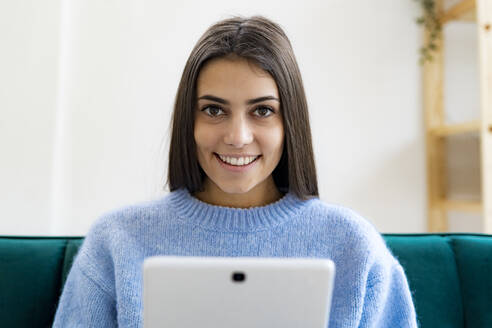 Junge Frau mit digitalem Tablet, lächelnd zu Hause sitzend - GIOF11209