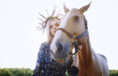 Frau mit Blumen, die ein Pferd gegen einen klaren Himmel hält - AZF00191