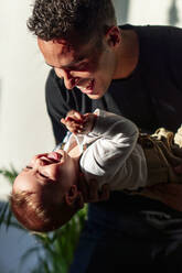 Verspielter Vater trägt Baby beim Spielen zu Hause - PGF00436