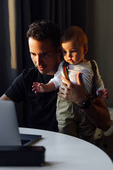 Father working on laptop while sitting with son at home - PGF00455