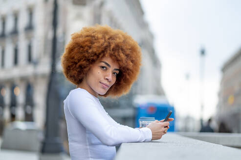 Curly hair woman using mobile phone while standing outdoors - OCMF02052