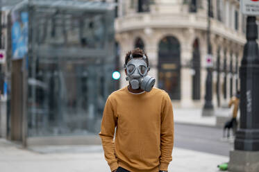 Man wearing protective gas mask standing with hands in pockets at city - OCMF02070