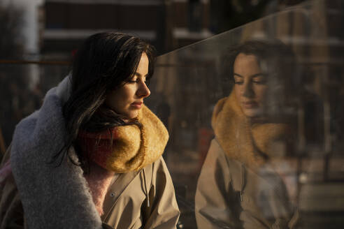 Beautiful woman in warm clothing looking through glass - AXHF00168