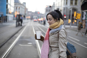 Schöne Frau mit Einwegbecher beim Überqueren der Straße im Winter - AXHF00172