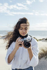 Junge Frau mit Vintage-Kamera am Strand an einem sonnigen Tag - JRVF00252