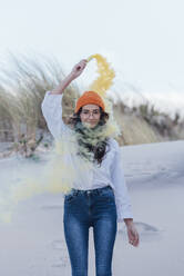 Young woman in orange knit hair with distress flare standing against sky at beach - JRVF00275