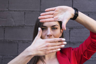 Geschäftsfrau mit grauen Augen macht Finger Rahmen gegen lila Backsteinwand - PNAF00637