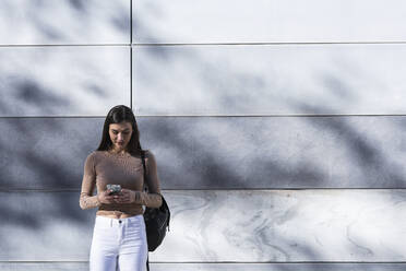 Eine Unternehmerin benutzt ein Mobiltelefon, während sie an der Wand steht - PNAF00645