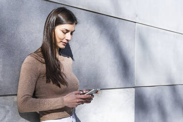 Smiling female entrepreneur using smart phone while leaning on wall - PNAF00646