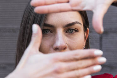 Woman with gray eyes making finger frame against wall - PNAF00651