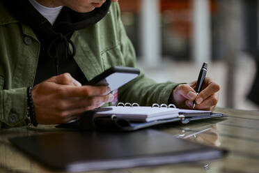 Man with mobile phone checking list in diary at table - ACPF01124