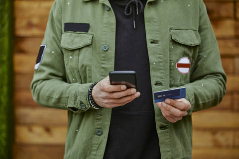 Man in jacket holding smart phone while doing online payment through credit card stock photo